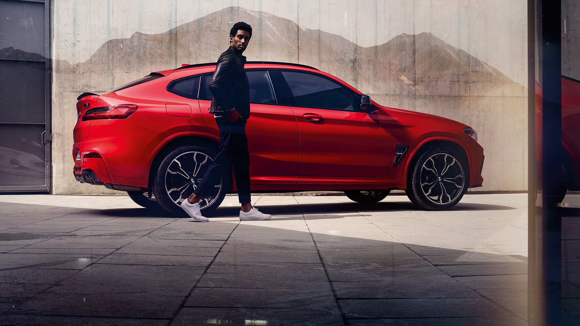 BMW X4 M Competition, vy från sidan med ung man. BMW X4 M Competition i Torontoröd metallic, Exteriör, vy från sidan med ung man.