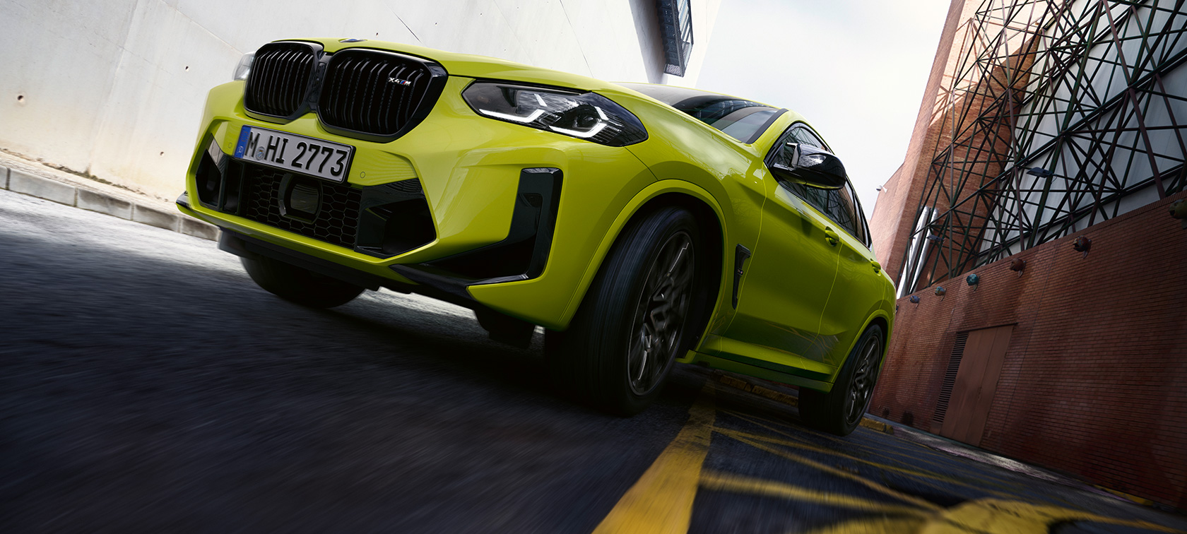 Vy snett underifrån och framifrån BMW X4 M Competition F98 LCI 2021 BMW X4 M Competition F98 LCI Facelift 2021 Sao Paolo-gul sedd snett underifrån från sidan körandes mellan huskroppar.