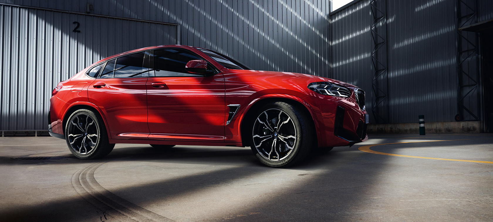 Vy snett framifrån BMW X4 M F98 LCI Facelift 2021 BMW X4 M F98 LCI Facelift 2021 Torontoröd metallic sedd framifrån i fabrikshall