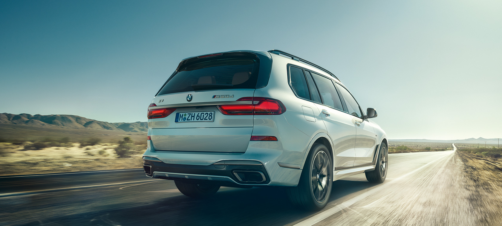 BMW X7 M50d, sedd bakifrån BMW X7 M50d i Mineralvit, körandes på tom motorväg, sedd bakifrån, G07, 2019