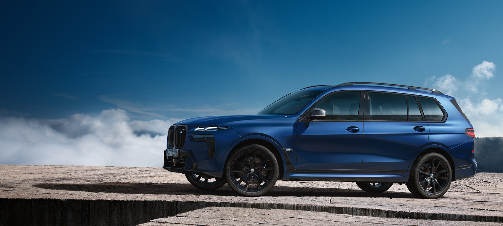 BMW X7 M60i xDrive G07 LCI Frozen Marina Bay Blue sidvy stillastående framför bergslandskap