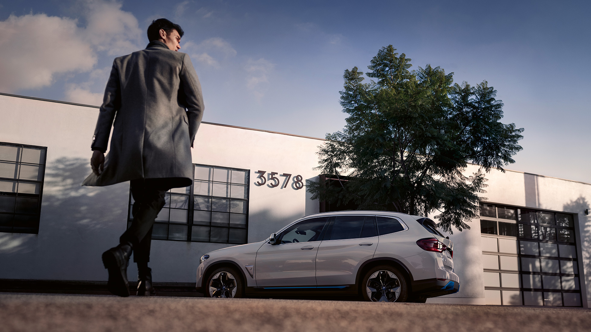 BMW iX3 G08 sedd från sidan framför byggnad med man BMW iX3 G08 2020 Mineralvit metallic vy från sidan framför byggnad med man