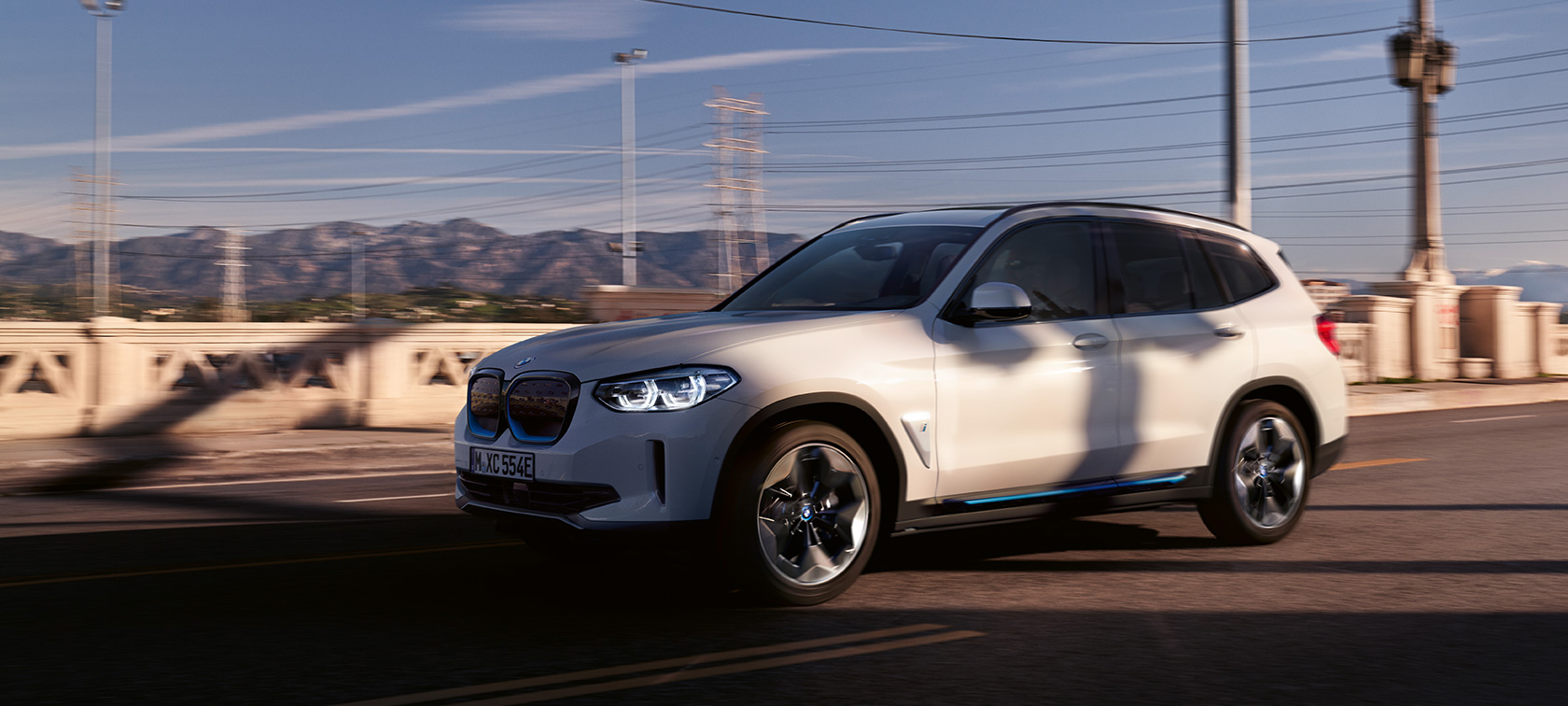 BMW iX3 G08 sedd snett framifrån i aktion på gatan BMW iX3 G08 2020 Mineralvit metallic sedd snett bakifrån i aktion på gatan