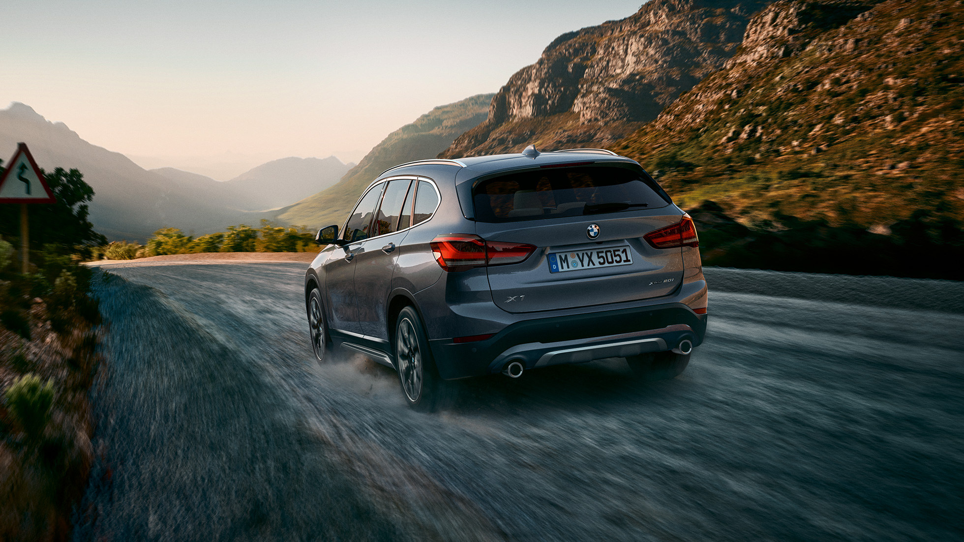 BMW X1, trefjärdedelsvy bakifrån. BMW X1, trefjärdedelsvy bakifrån, körande framför berglandskap.