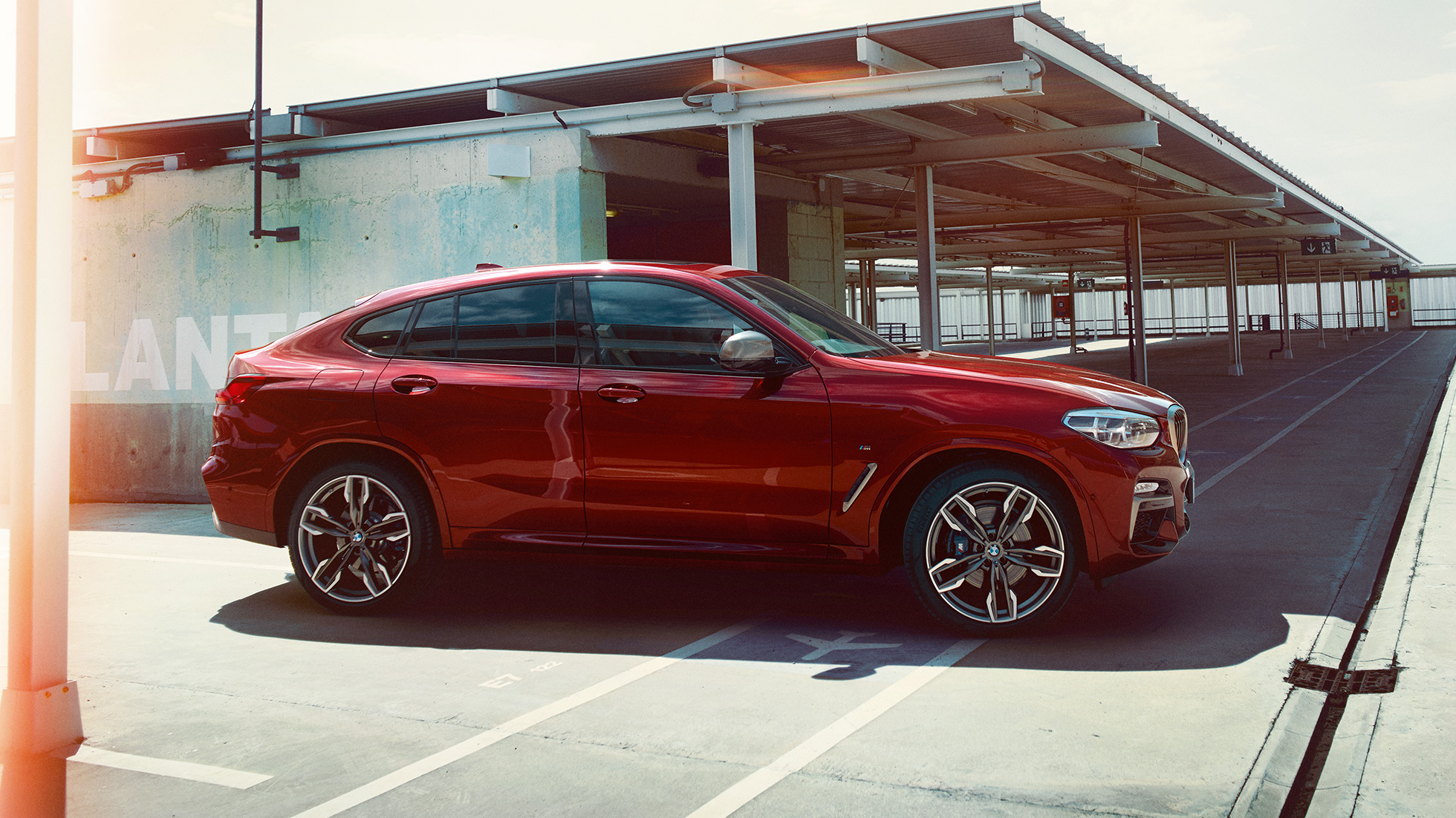 Sportig silhuett. BMW X4 Sportig silhuett BMW X4 M40i G02 2018 Flamencoröd briljanteffekt röd sedd från sidan