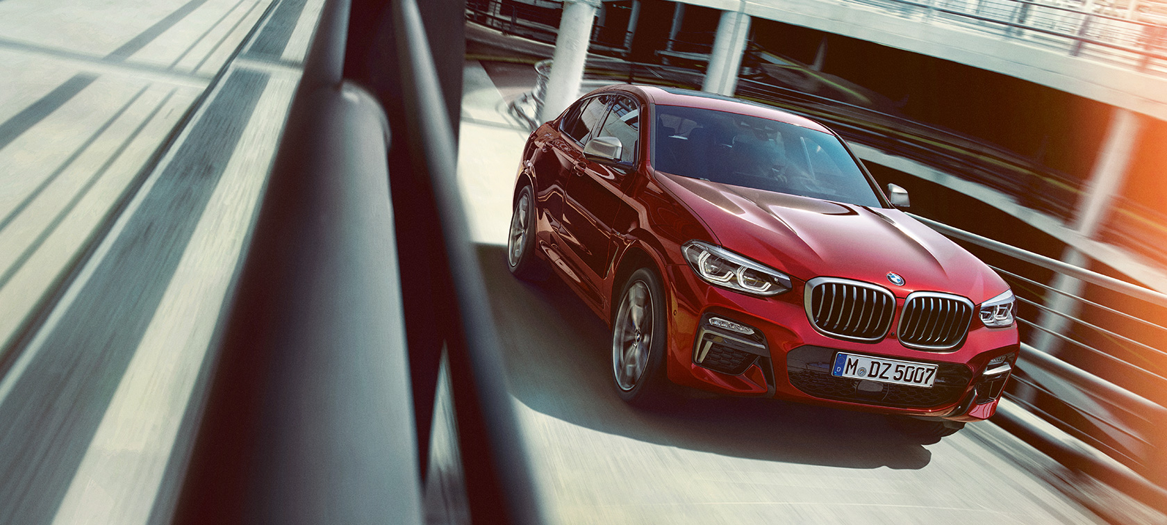 BMW X4 körandes i parkeringshus BMW X4 G02 2018 Flamencoröd briljanteffekt trefjärdelsvy från sidan körandes i parkeringshus