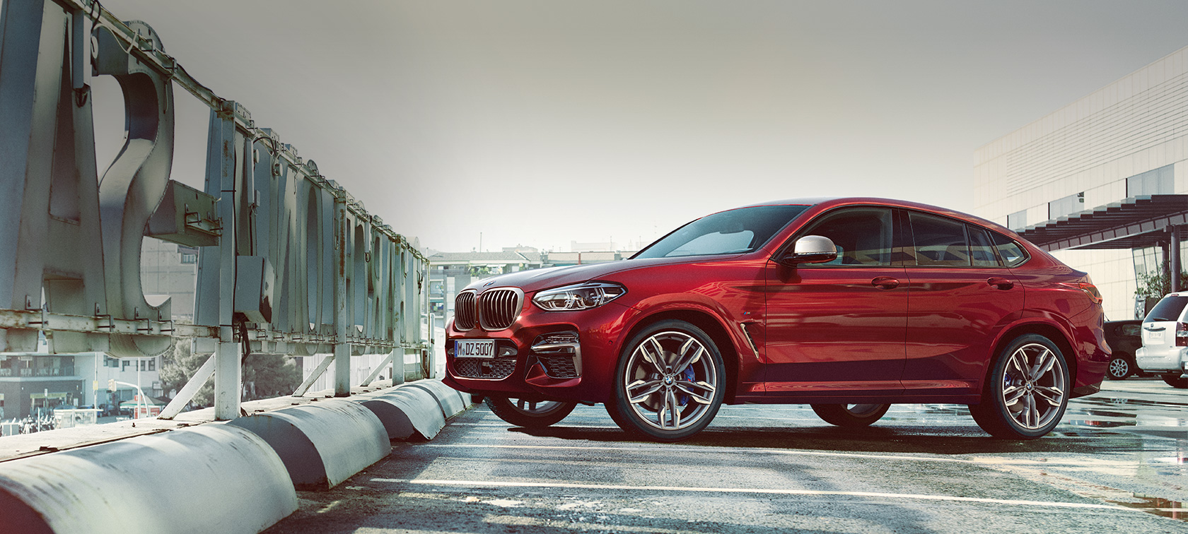BMW X4 sedd från sidan parkerandes BMW X4 M40i G02 2018 Flamencoröd briljanteffekt sedd från sidan i parkeringshus