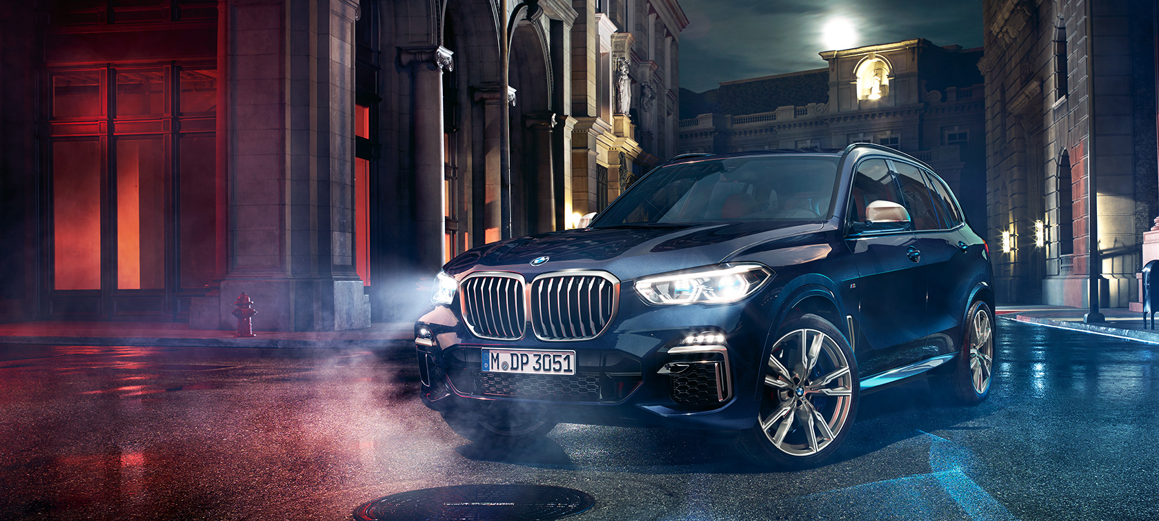 BMW X5 M50d på vägen BMW X5 M50d står på en gata framför en storstadskuliss på natten