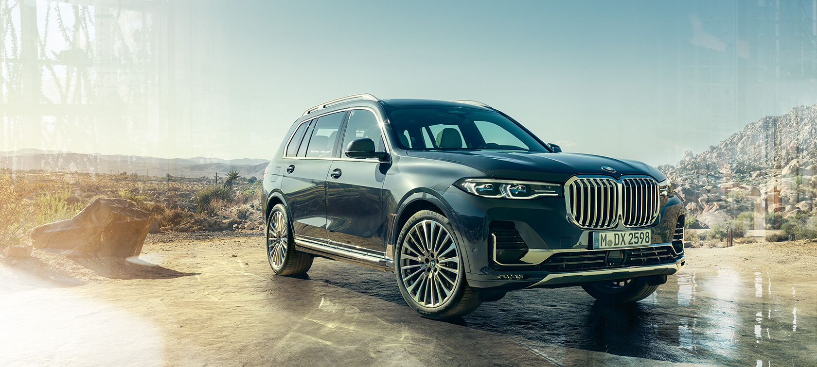 BMW X7, trefjärdedelsvy framifrån. BMW X7 i Arctic Grey parkerad framför öken, trefjärdedelsvy framifrån vänster sida, G07 2019