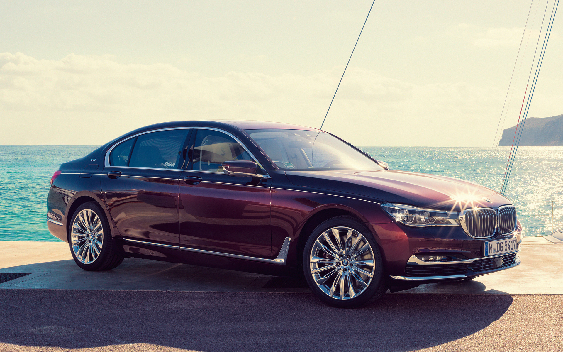 BMW Individual M760Li inspired by Nautor’s Swan G1 2017 framför en segelbåt BMW Individual M760Li inspired by Nautor’s Swan G12 2017, snett från sidan, stående vid piren framför en segelbåt i en vik