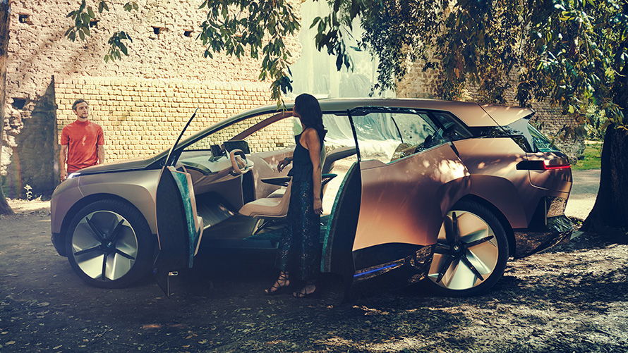 Sida av BMW Vision iNEXT Sidan av BMW Vision iNEXT med en kvinna vid den öppna dörren och en man i bakgrunden