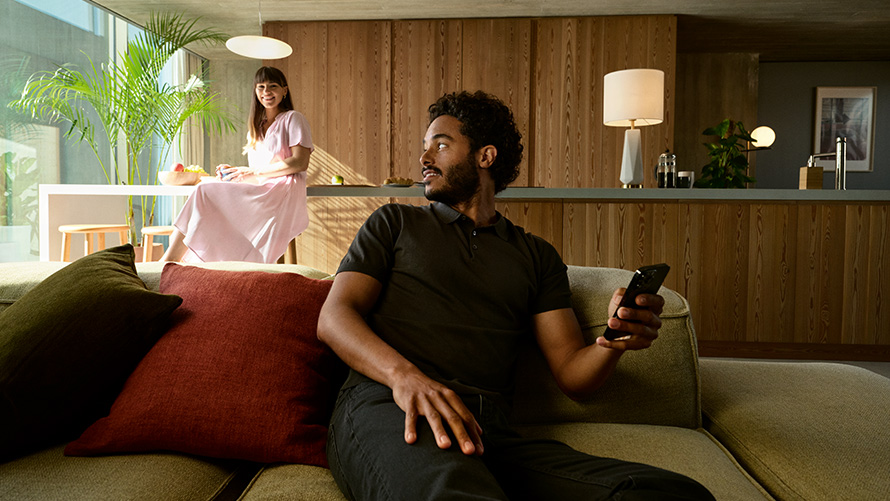 Delning BMW Digital Key BMW Digital Key delning man med smartphone i handen sitter i en soffa med kvinna i bakgrunden