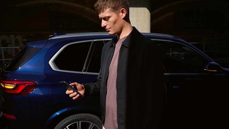 BMW Digital Key – installera för upp till fem användare Installera BMW Digital Key för upp till fem användare, man med smart telefon framför en BMW X5
