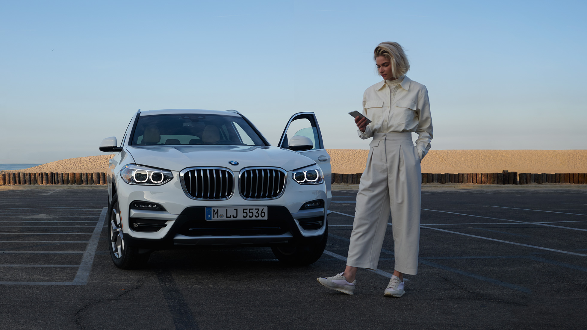 Kvinna använder My BMW-appen på sin smartphone Kvinna använder My BMW-appen i BMW ConnectedDrive på sin smartphone framför en vit BMW X5