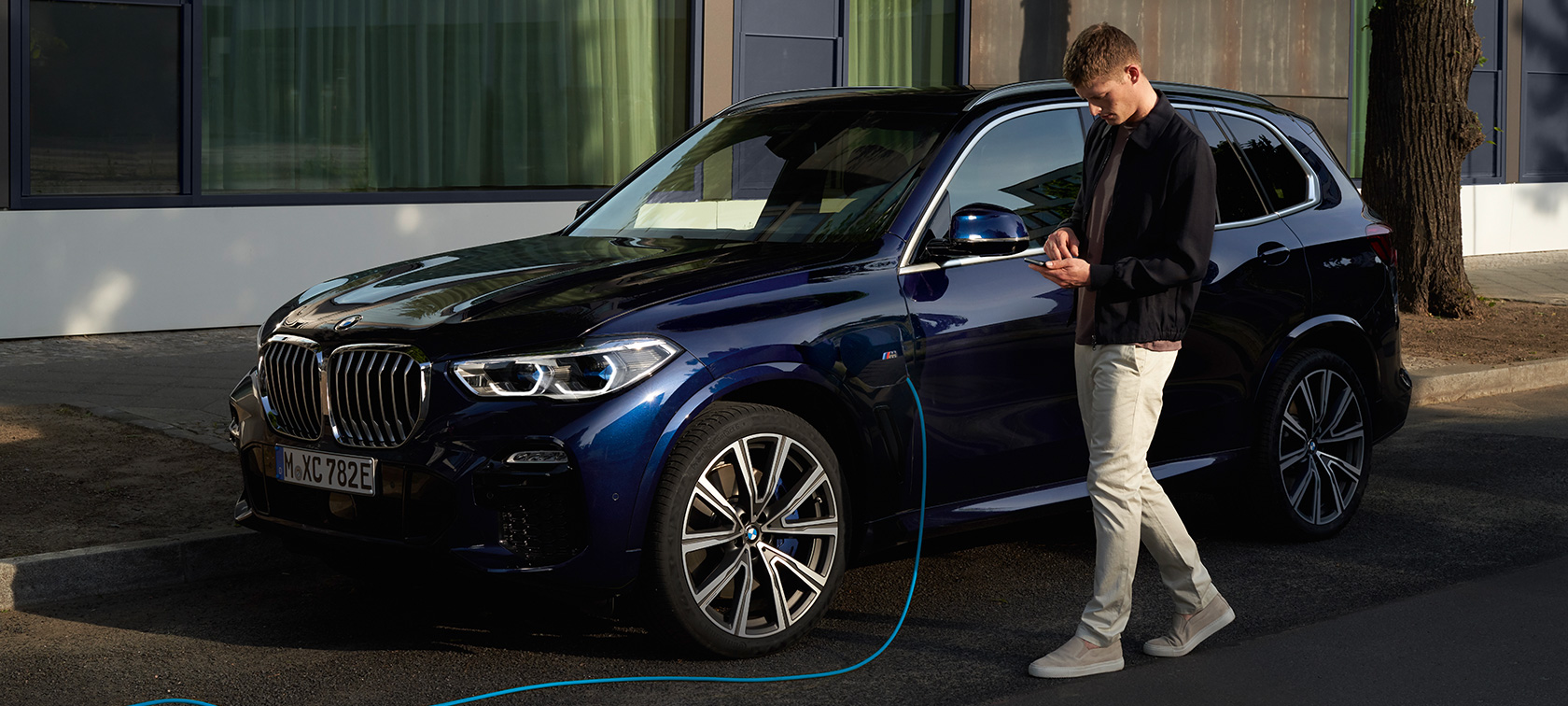 Man använder My BMW-appen på sin smartphone Man använder My BMW-appen i BMW ConnectedDrive medan hans BMW X5 laddhybrid laddas