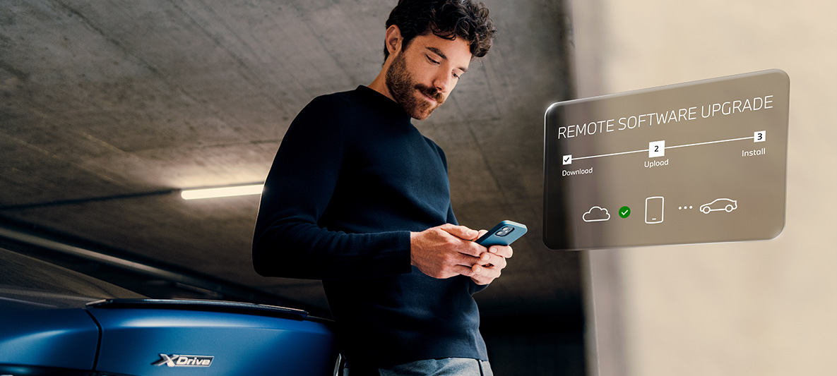 En man lutar sig mot bakpartiet på en BMW och tittar på sin smartphone Remote Software Upgrade en man lutar sig mot bakpartiet på en BMW och tittar på sin smartphone