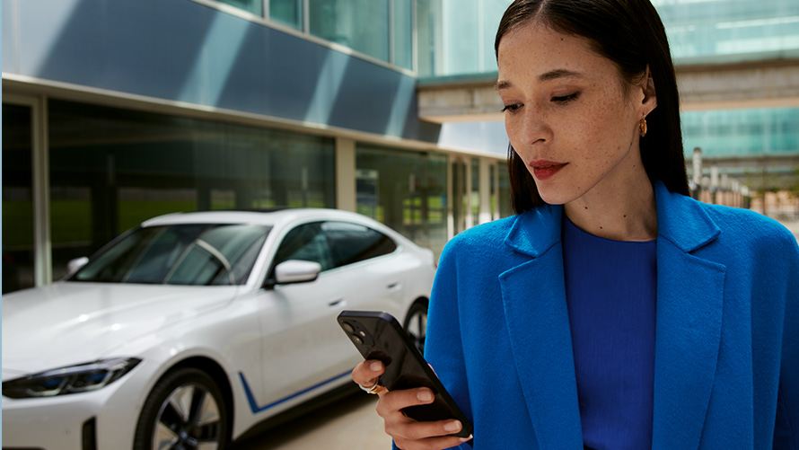 En kvinna står framför en BMW En kvinna står framför en BMW och tittar på sin smartphone