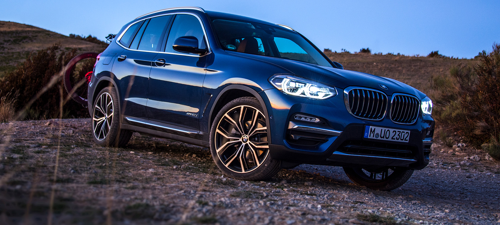 Mörkblå BMW X3 i terräng Stillastående mörkblå BMW X3 med cykelhållare och mountainbike i terräng
