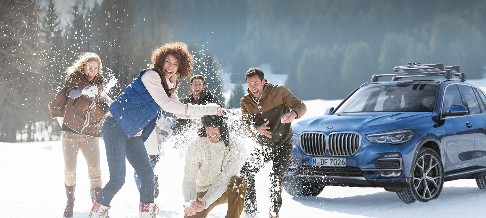 BMW Originaltillbehör och BMW Service för höst och vinter. Kvinnor och män som skrattar i snön framför en BMW