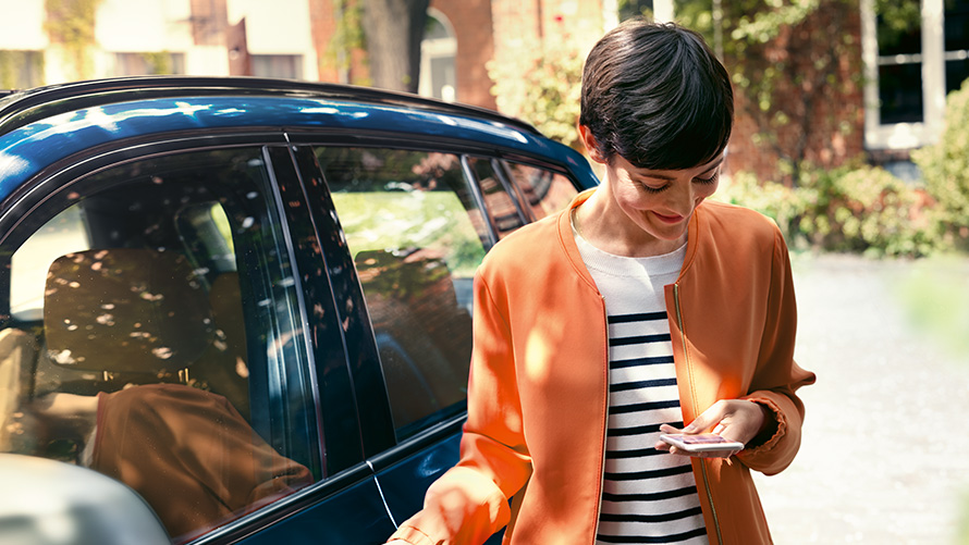 BMW erbjudande sommar BMW Teleservices BMW erbjudande sommar BMW Teleservices kvinna står framför en BMW och använder sin smartphone