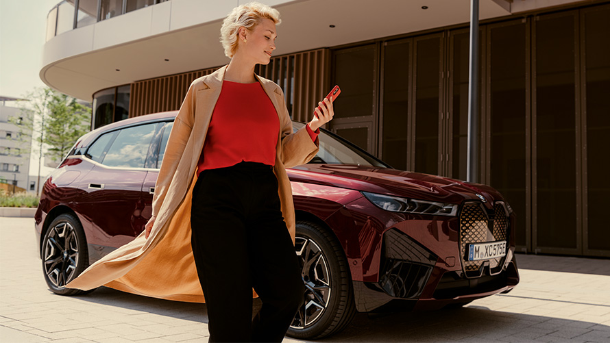 Appen My BMW kvinna med smartphone framför en BMW Kvinna med smartphone framför en BMW