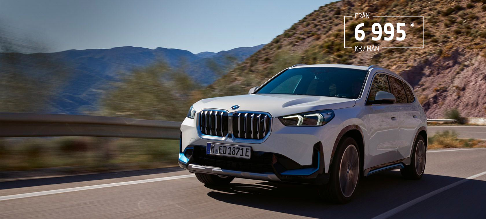 BMW iX1 U11 BEV 2022 Mineralvit metallic sedd körandes snett framifrån på en slingrande bergsväg