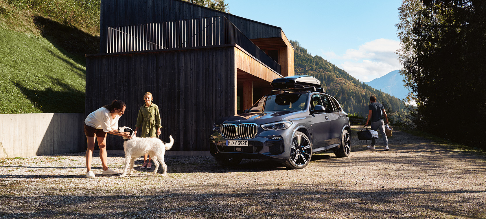 Familj med hund framför en BMW som parkerat framför ett hus i sommarmiljö. Familj med hund framför en BMW som parkerat framför ett hus i sommarmiljö.