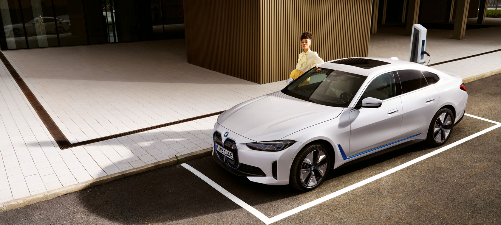 BMW i4 eDrive40 G26 2021 Mineralvit sedd snett framifrån parkerad vid havet med kullar i bakgrunden