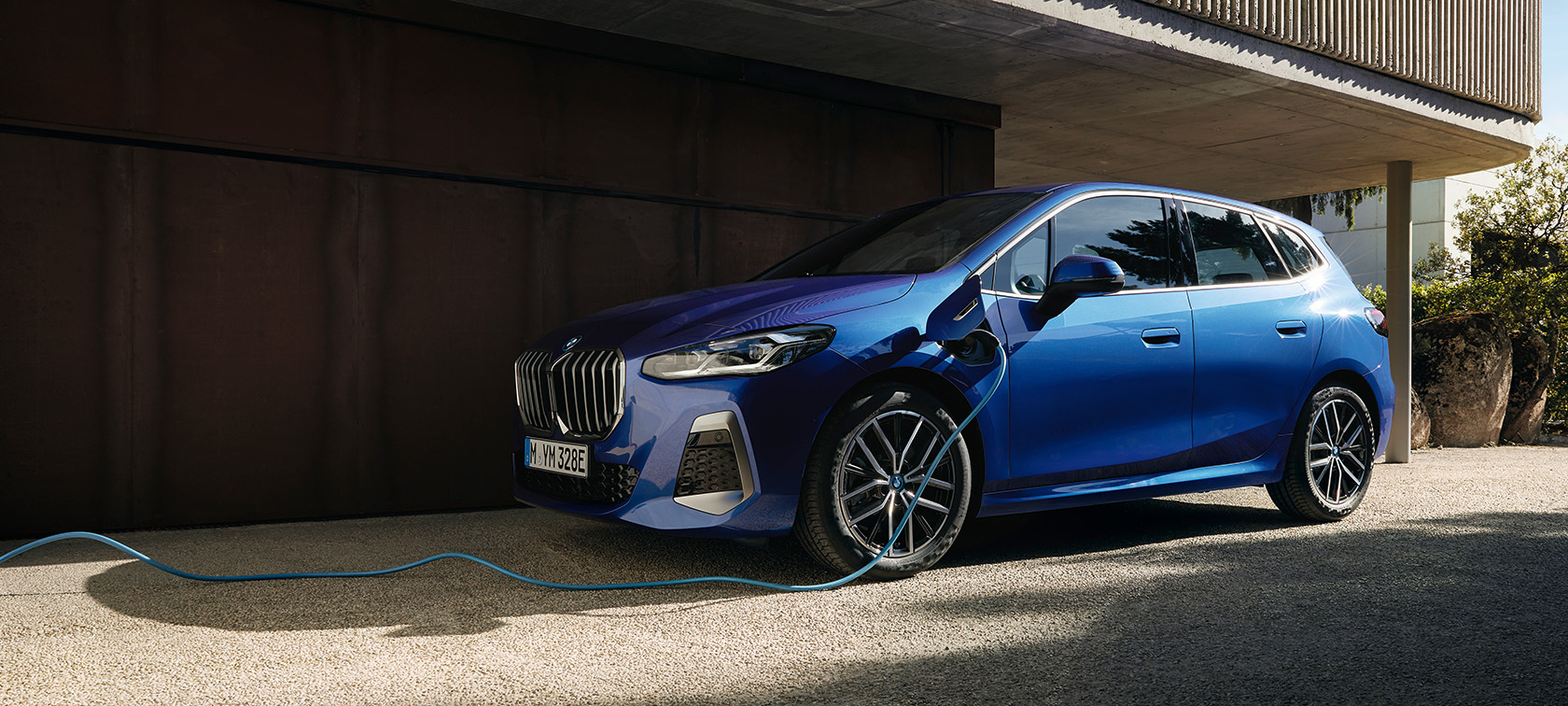 BMW 2-serie Active Tourer 230e laddhybrid U06 2021 Portimao Bl&aring; metallic sedd snett framifr&aring;n vid laddstolpen