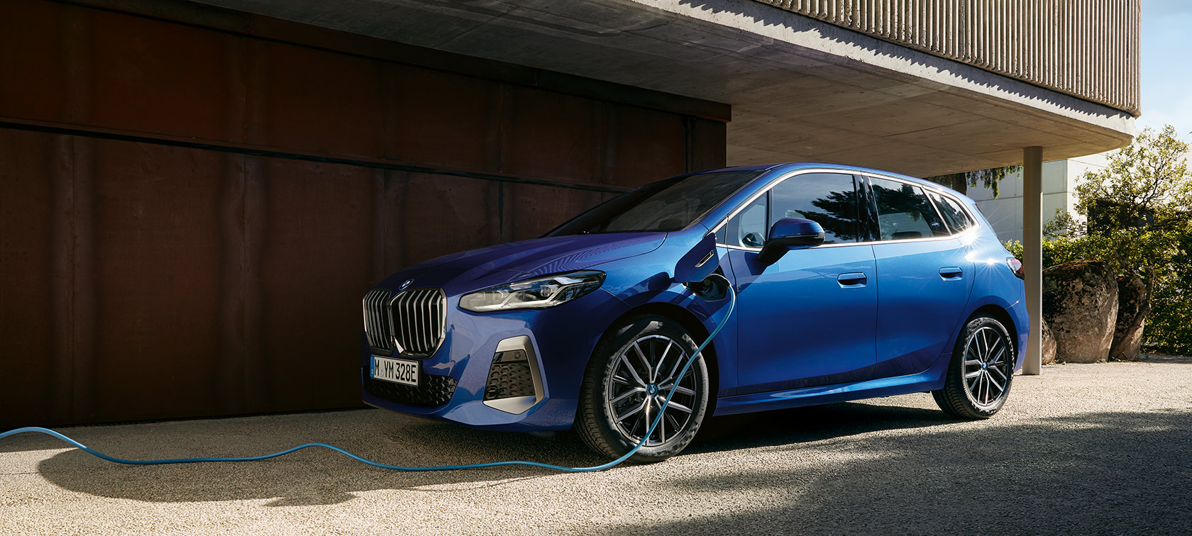 BMW 2-serie Active Tourer 230e laddhybrid U06 2021 Portimao Bl&aring; metallic sedd snett framifr&aring;n vid laddstolpen