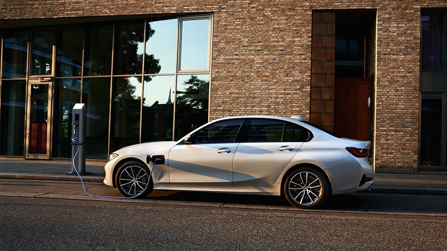 En vit BMW 3-serie Sedan laddhybrid som laddas vid en laddstolpe