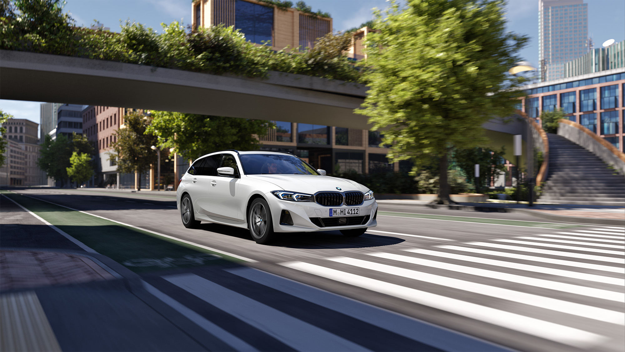 En vit BMW 3-serie Touring sedd snedd framifrån körandes på en väg i stadsmiljö