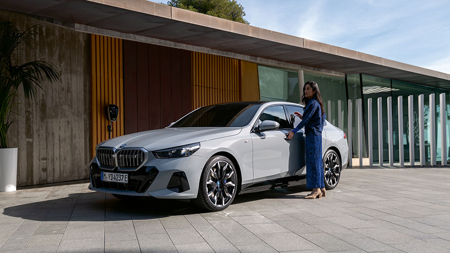 En ljusgrå BMW i5 Sedan sedd från från sidan parkerad framför ett hus