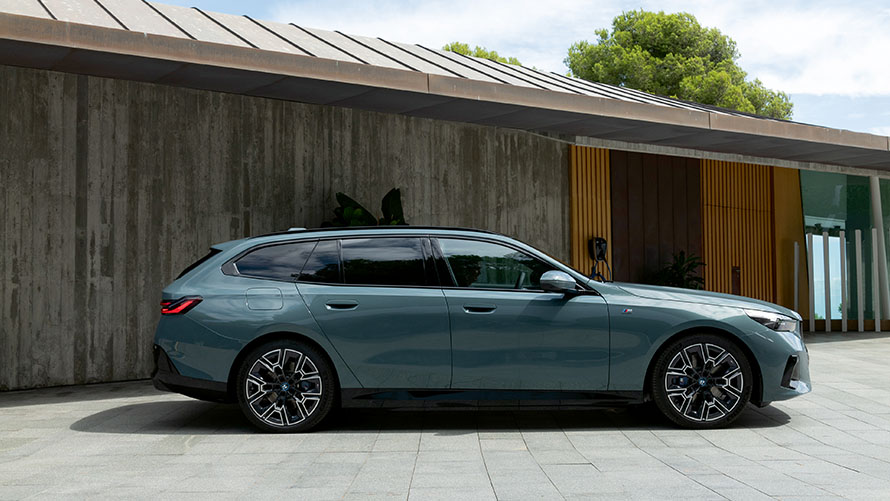 En blå BMW i5 Touring sedd från sidan parkerad framför ett hus