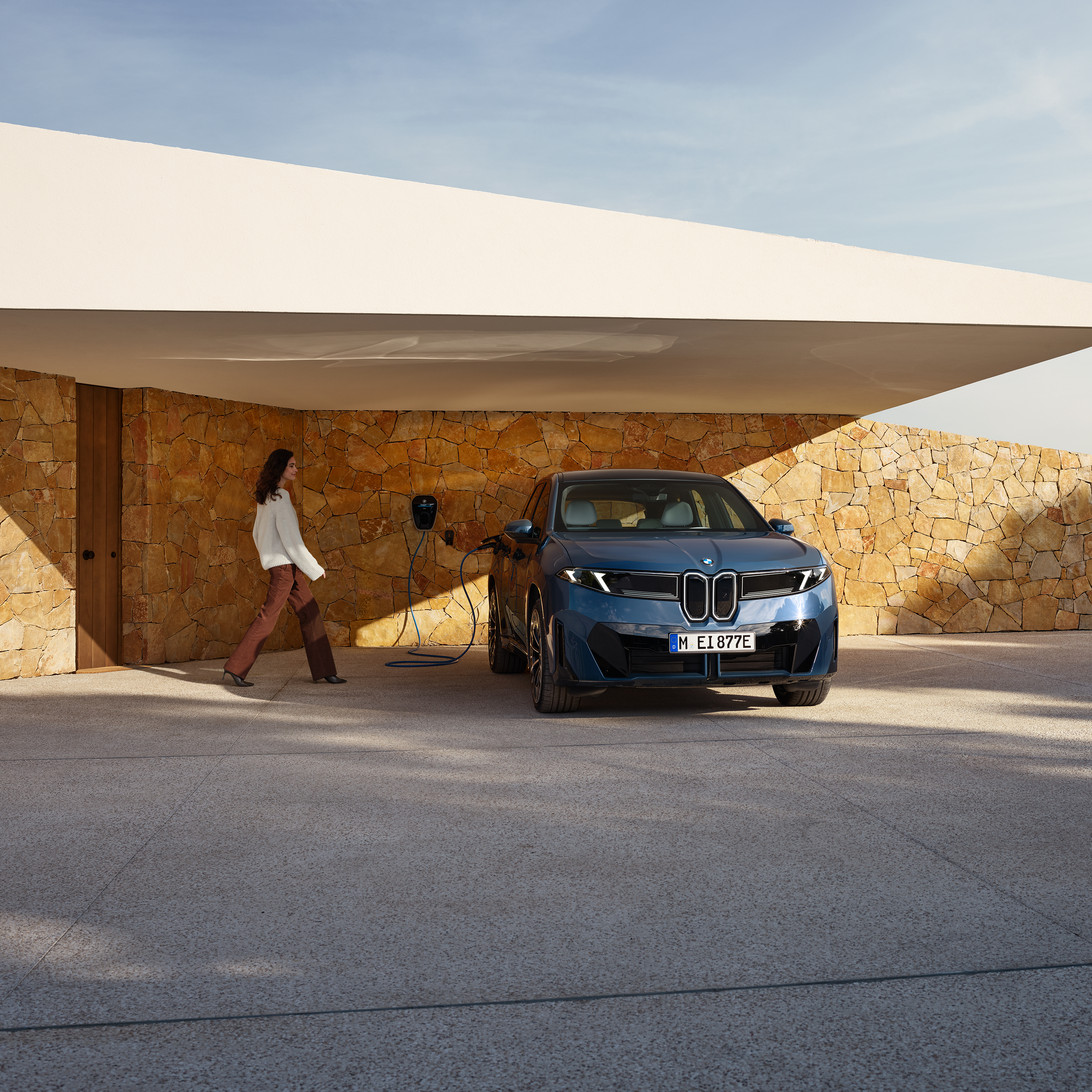 En kvinna går mot en BMW iX3 ansluten till en laddbox