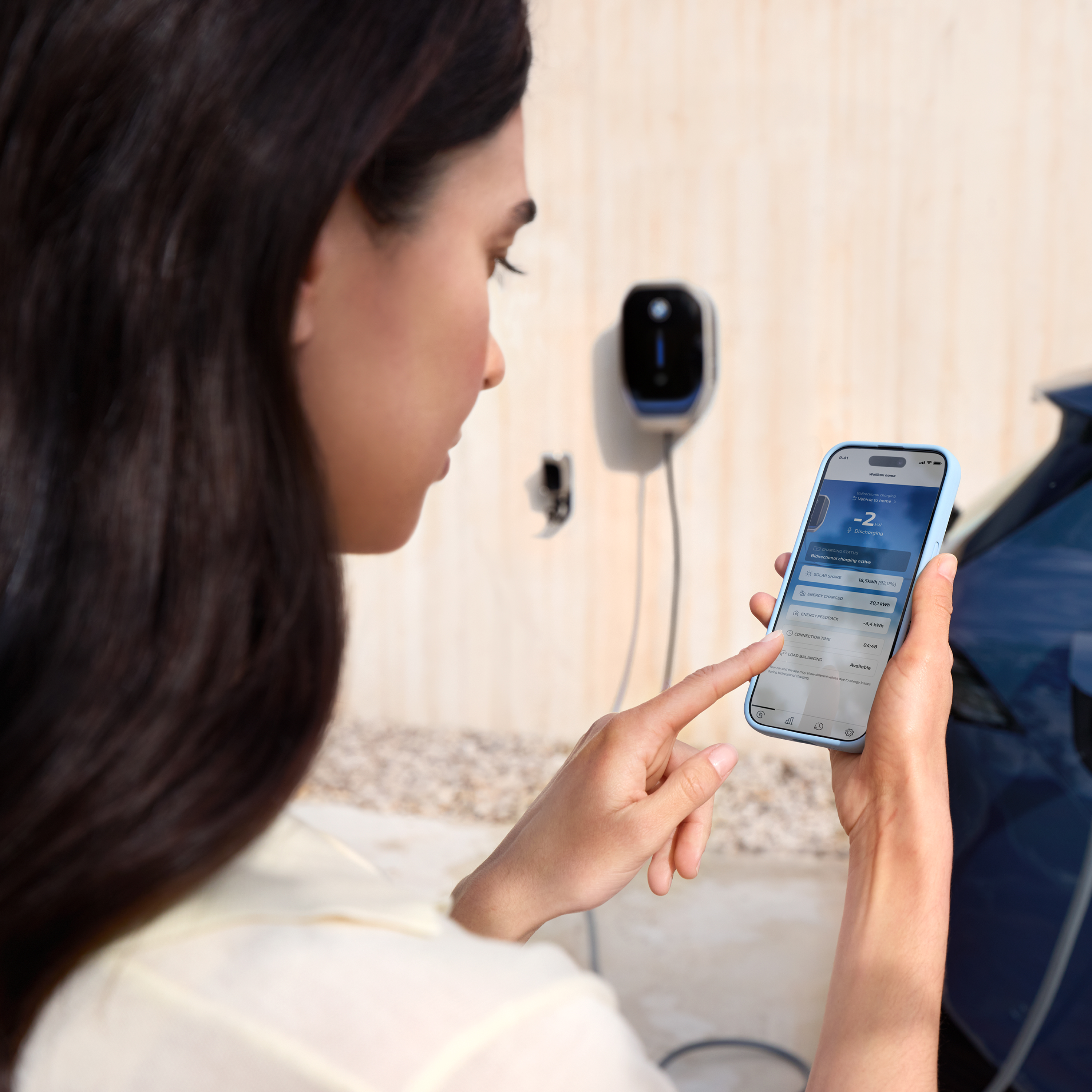 En kvinna tittar på sin smartphone, en laddbox syns i bakgrunden