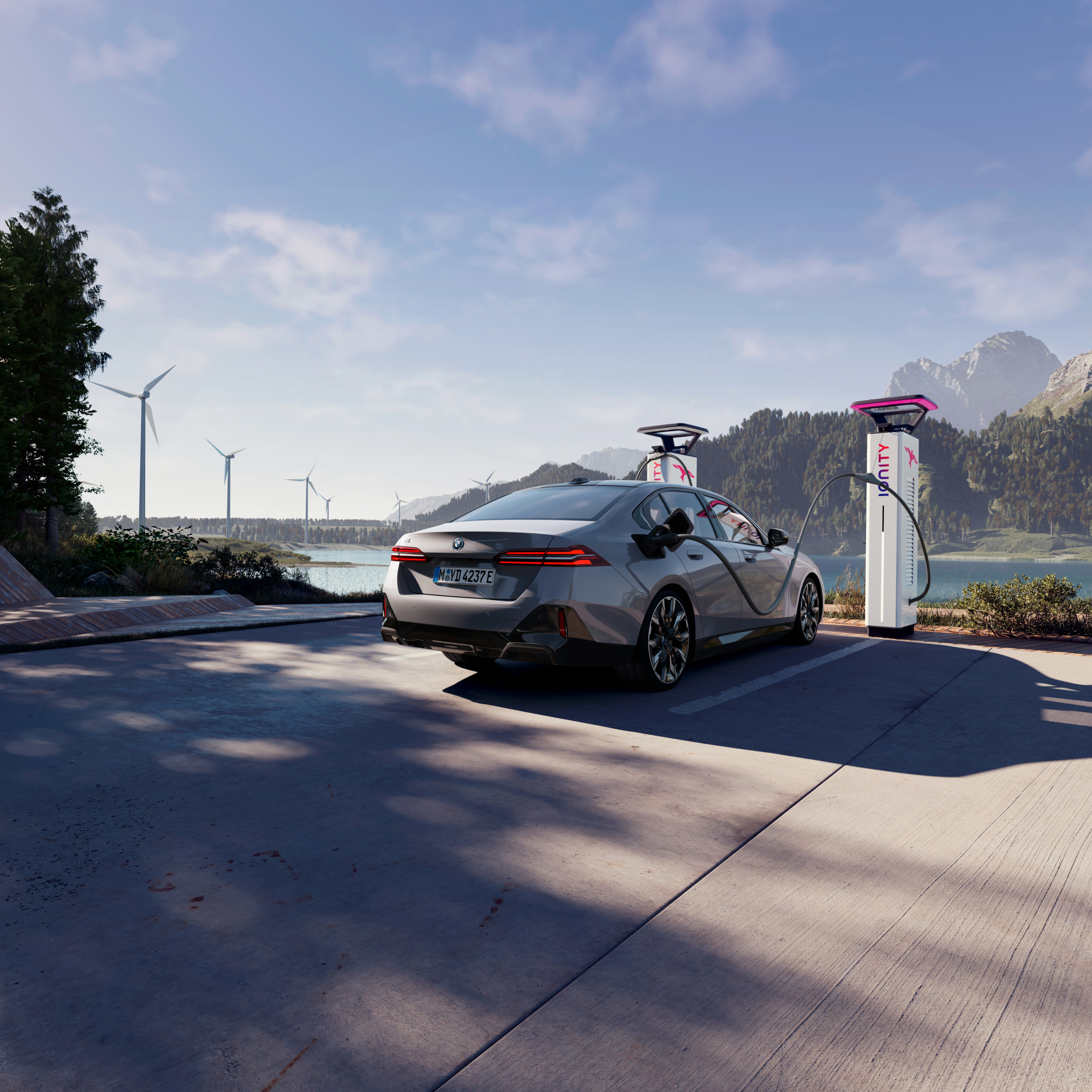 BMW laddar vid en laddstation med utsikt över vatten, berg och vindkraftverk